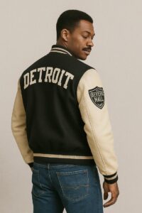 A man showing the back of the Axel Foley Detroit jacket featuring “DETROIT” lettering and a Beverly Mall patch on the sleeve.