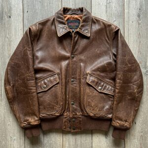 A vintage brown leather bomber jacket with distressed texture and button front closure.