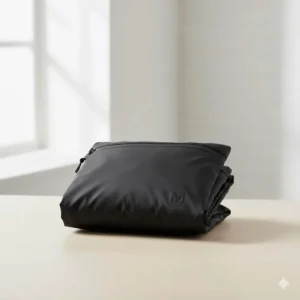 A women's black rain jacket folded into its own compact carrying pouch for easy travel storage.