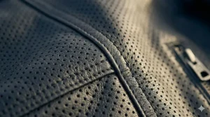 Detailed shot of heavy-duty safety stitching on the seams of a perforated leather motorcycle jacket.