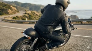 A motorcyclist in a leaning riding position wearing a perforated leather jacket with accordion stretch panels.